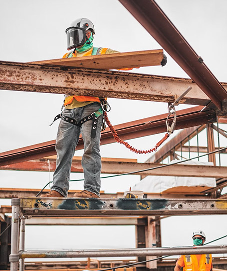 A construction worker standing on a high-beam with fall-protection gear attached.