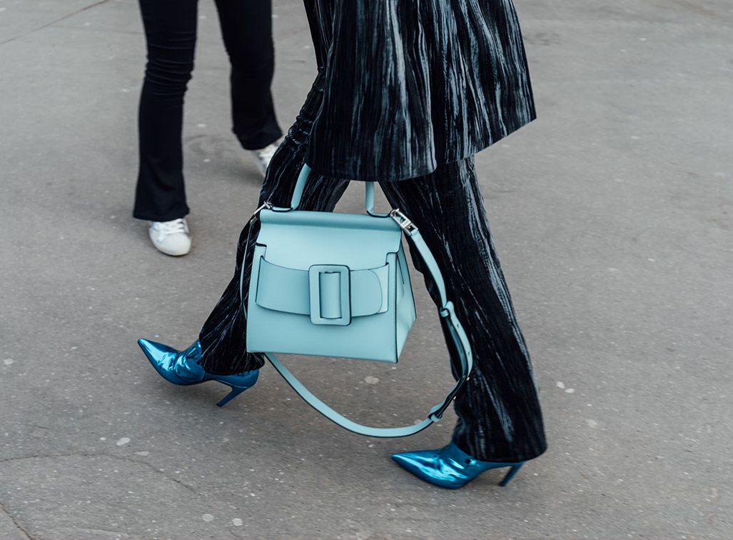 A stylish woman in a leather pant-suit holding a designer turquoise bag.